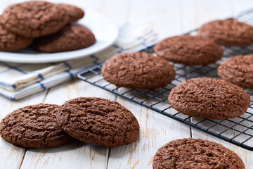 Traditional chocolate cookies are cooling after baking on a rack on a white table, selective focus.