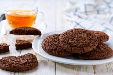 Tasty chocolate brownie cookies with cracks  and tea on a light kitchen table, selective focus.