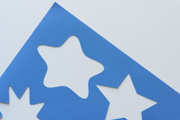 corner of a stencil with star shapes machine-cut from blank blue paper and arranged on blank paper