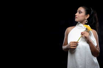 solo image of a beautiful indian female model in a white shirt white top white dress holding a yellow flower