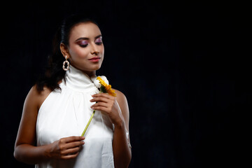 solo image of a beautiful indian female model in a white shirt white top white dress holding a yellow flower