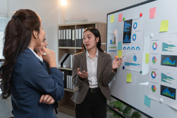 Asian businesswomen discussing charts and graphs on whiteboard during a presentation in the office meeting room, teamwork and collaboration concept