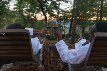 Homosexual LGBT male couple enjoying a resort weekend, relaxing after a hot tub treatment, tasting and drinking red wine on a terrace.