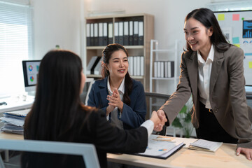 Businesswomen shaking hands and smiling while sitting at office desk after successful meeting, demonstrating teamwork and collaboration