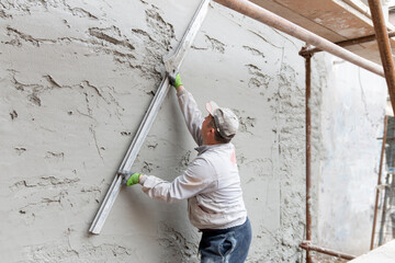 A worker hand removes excess plaster with leveler and spatula. Renovation
