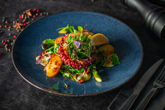 A vibrant octopus dish served with roasted potatoes, greens on a blue plate