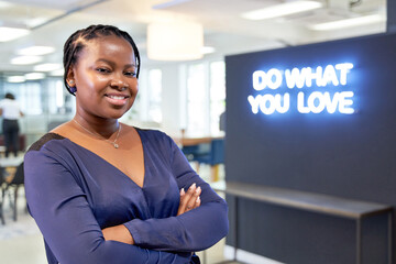 Attractive unique African American female with blue blouse smiling at camera near trendy neon sign