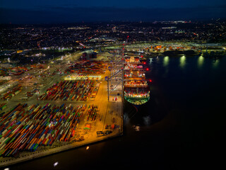 Illuminated Southampton UK container terminal with large container ship at night. High altitude...