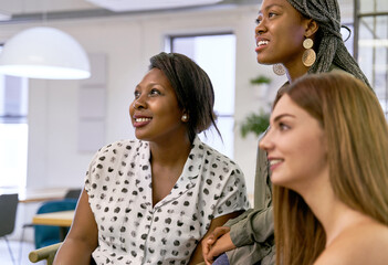 Diverse group of three young attractive multi-ethnic professional female coworkers looking into distance together in office