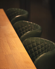 Three dark green kitchen chairs lined up against a wooden breakfast bar in a cosy home interior