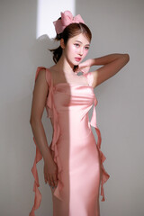 Stylish young fashionable Asian woman in a stunning pink dress, trendy makeup with light shining...