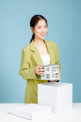 Young successful investor business woman in casual suit holding house model at white office desk with pc laptop isolated on pastel blue background studio portrait. Achievement concept