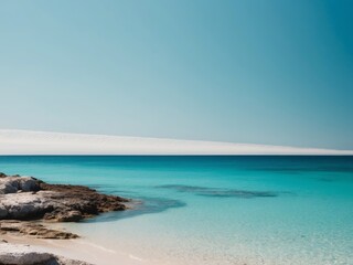 Obraz premium Tranquil beach scene with rocky shoreline and clear blue sea under a clear sky.