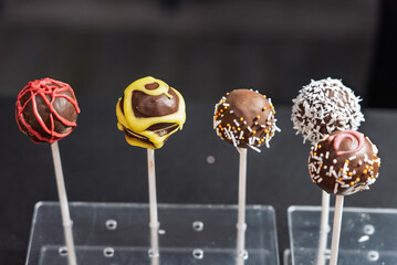 Decorative chocolate pops on sticks with vibrant colors and toppings arranged on a clear display...