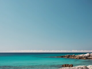 Obraz premium Tranquil beach scene with rocky shoreline and clear blue sea under a clear sky.