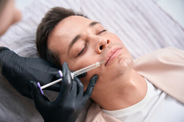Top view woman cosmetologist doing injections of filler into male client lips