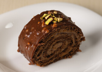 A chocolate roll covered with glossy nut glaze and garnished with pistachios