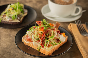 A close-up of a gourmet toast topped with fresh vegetables, prosciutto, cream