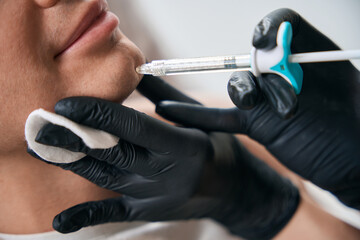 Skilled beautician making filler injections into handsome client cleft chin