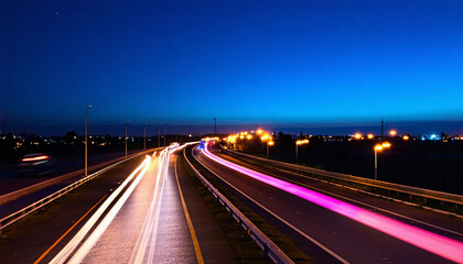 A long-exposure photograph of a highway at night, showing colorful light trails of cars speeding by