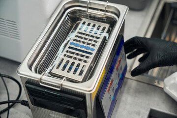 Male technician adjusting ultrasonic bath machine to clean dental instruments