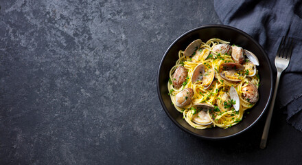Spaghetti with clams, seafood pasta alle vongole in a black bowl. Dark background. Copy space. Top view.