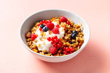 Healthy breakfast. Granola, muesli with yogurt and fresh berries. Pink background. Close up.