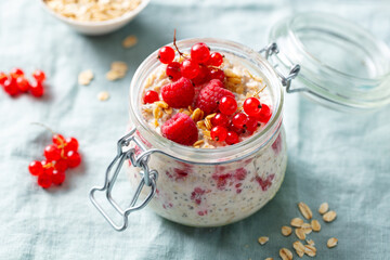 Overnight oats with fresh raspberries and red currants in glass jars. Blue textile background. Close up.