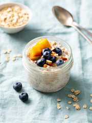 Overnight oats with fresh berries and fruits in glass jars. Blue textile background. Close up.