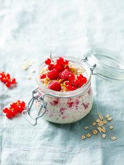 Overnight oats with fresh raspberries and red currants in glass jars. Blue textile background. Copy space.