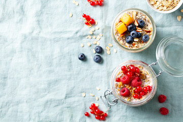 Overnight oats with fresh berries and fruits in glass jars. Blue textile background. Copy space. Top view.