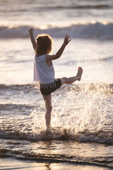 Child plays joyfully in ocean waves at sunset on warm summer evening