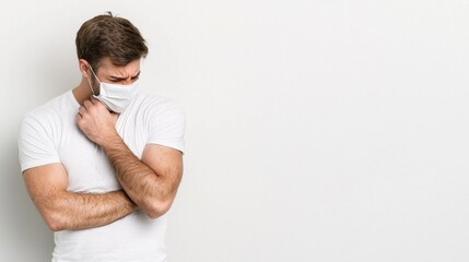 Young Man in White T-Shirt Wears Protective Face Mask and Stands Against Minimalist Background, Expressing Concern and Uncertainty About Health and Safety Measures