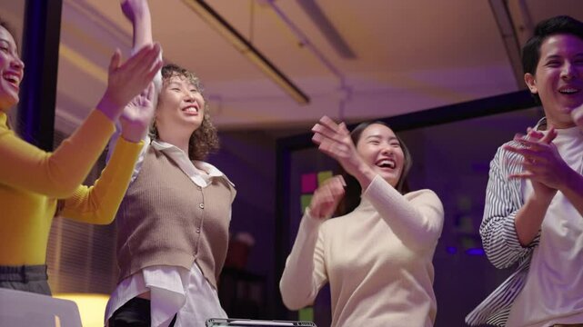 Young Asian business team stacking hands and raising them together and clasping hands after show of teamwork and success, celebrating their achievement with enthusiasm