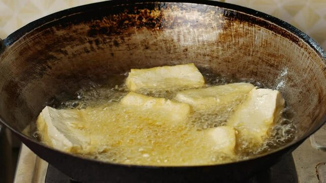 4k video of frying tofu in a pan filled with cooking oil.