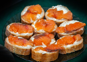 Sandwiches made of white bread, butter and pieces of red salted fish in close-up on a dark background