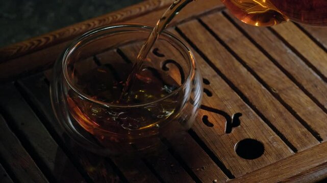 Tea ceremony on dark background. Pouring red/black tea in cup. 