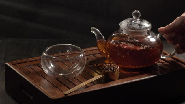Tea ceremony on dark background. Pouring red/black tea in cup. 