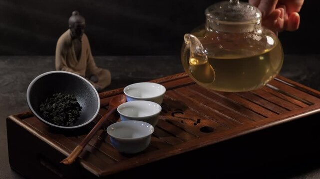 Tea ceremony on dark background. Pouring green tea in cup. 