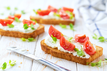 Traditional Italian appetizer, bruschetta with ricotta cheese and cherry tomatoes on a wooden table.