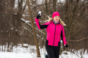 Redhead girl in black track suit running and looking at her phone. Winter landscape in background. 