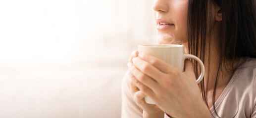 Coffee break time. Unrecognizable millennial girl holding cup of hot beverage at home, closeup view. Copy space. Panorama