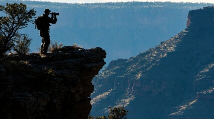 Obraz premium Silhouette of a Photographer Standing on a Rock Edge Capturing Scenic Views of Mountains and Valleys in the Early Morning Light