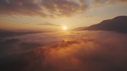 Fototapeta premium Breathtaking Aerial View of a Misty Mountain Sunrise with Soft Golden Light Illuminating Rolling Hills and a Sea of Clouds in a Serene Landscape
