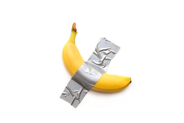 The banana is taped with grey tape to a white wall