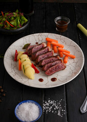 Grilled beef steaks and vegetables, With cooked carrots and mashed potatoes, black wood background