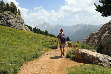 Fototapeta premium woman hiker with backpack walking on dirt trail in mountains during spring