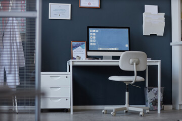 Background image of workplace in medical clinic with computer on desk against blue wall, no people, copy space