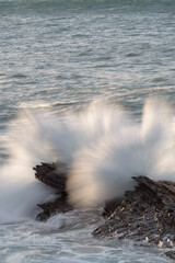 Wave crashing against a rock with a long exposure in the Cantabrian Sea, slightly bathed in the light of the evening sun