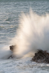 Wave crashing against a rock with a long exposure in the Cantabrian Sea, slightly bathed in the light of the evening sun